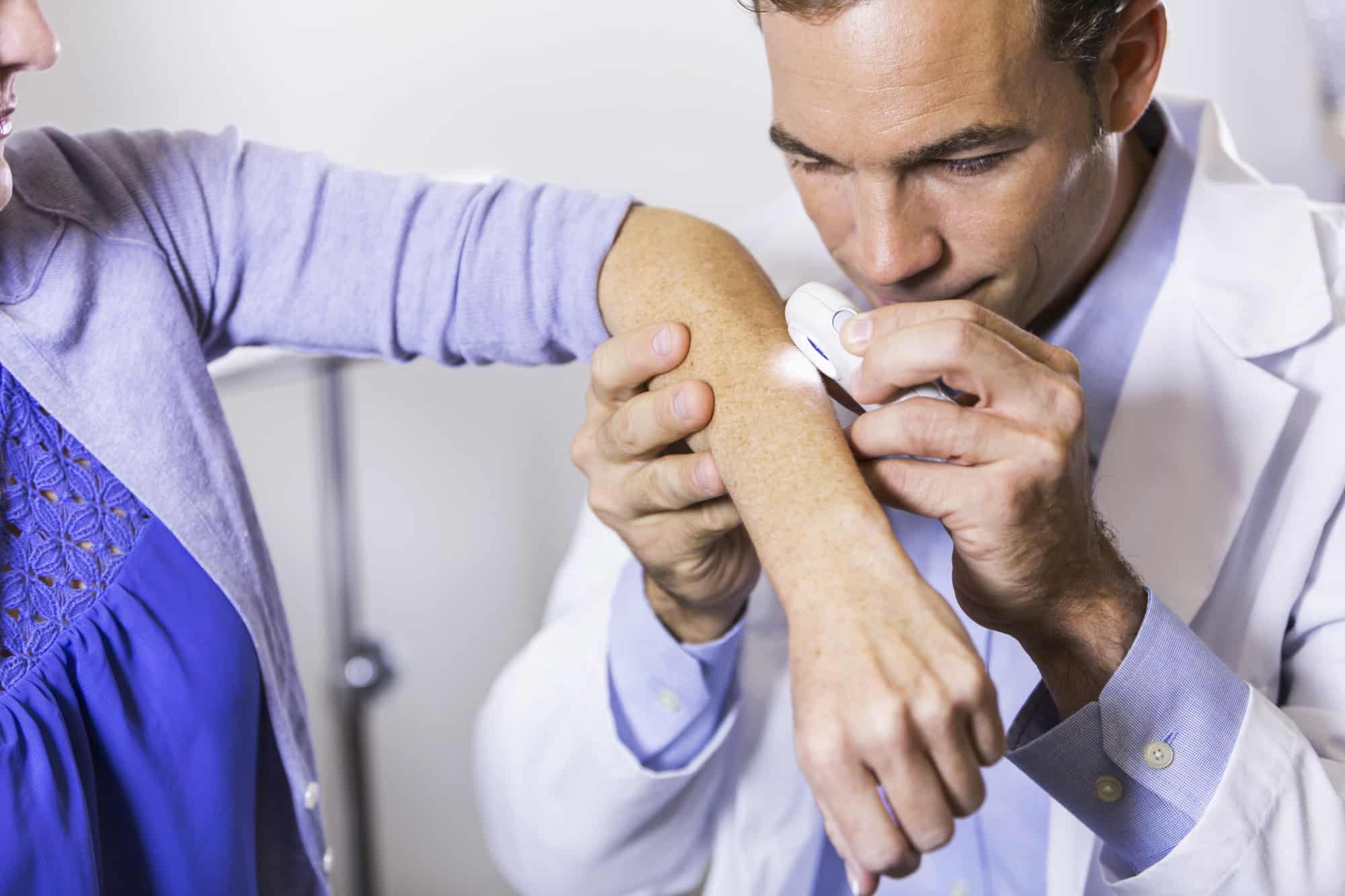 Dermatologist examining a patient's forearm with a handheld dermatoscope