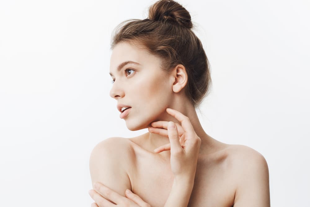 Woman with her hair in a bun and her hand at her neck