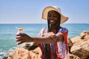 Young,African,American,Woman,Smiling,Happy,Using,Sunscreen,Lotion,At