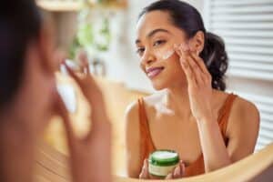 A woman looking in the mirror and applying cream to her skin as part of her skincare routine