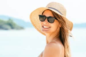 Woman smiling at the beach with hat and sunglasses to protect skin in Los Angeles