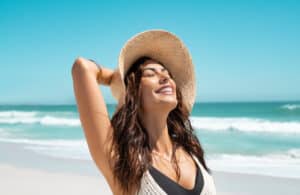 Woman on the beach smiling at the sun, needing sun protection in Los Angeles, CA